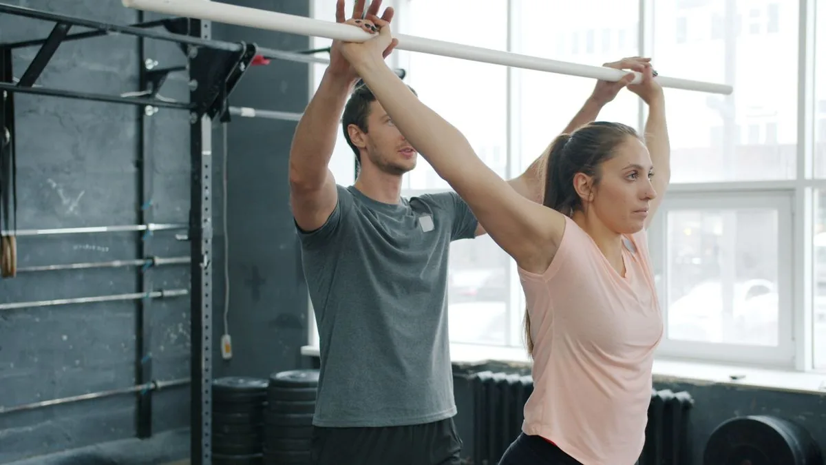 Un coach accompagne une pratiquante qui lève un bâton au-dessus de la tête.